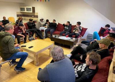 Skupina ľudí sediacich v kruhu v spoločenskej miestnosti pri diskusii.