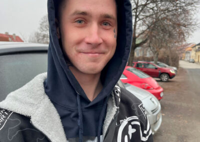 Mladý muž v čiernej mikine s kapucňou vonku pri aute.